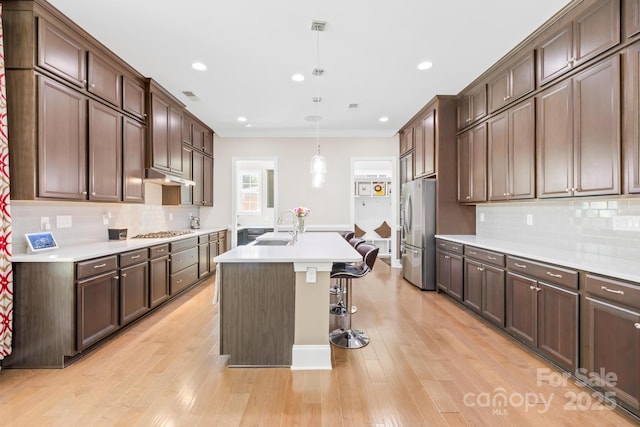 kitchen with appliances with stainless steel finishes, light countertops, a sink, a center island with sink, and light wood finished floors