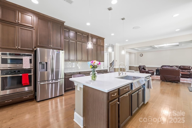 kitchen with stainless steel appliances, light wood finished floors, a sink, and decorative backsplash