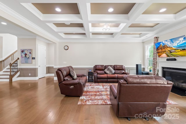 living area featuring a glass covered fireplace, ornamental molding, stairs, beam ceiling, and light wood finished floors