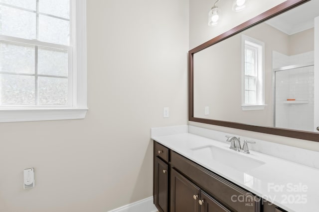 full bathroom with a shower with shower door, vanity, baseboards, and a wealth of natural light