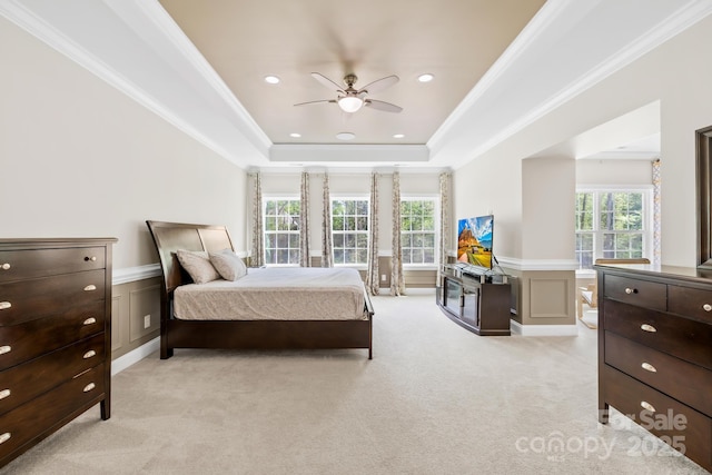 bedroom with a raised ceiling, light carpet, multiple windows, and wainscoting