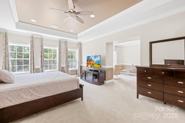 bedroom with ornamental molding, a tray ceiling, a wainscoted wall, and light carpet