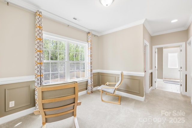 living area with visible vents, a decorative wall, carpet, crown molding, and wainscoting