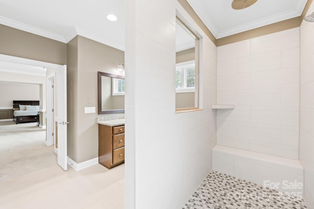 bathroom with vanity, a tile shower, baseboards, and crown molding