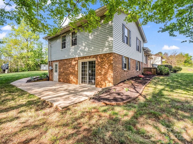 back of house featuring a patio area, brick siding, and a yard