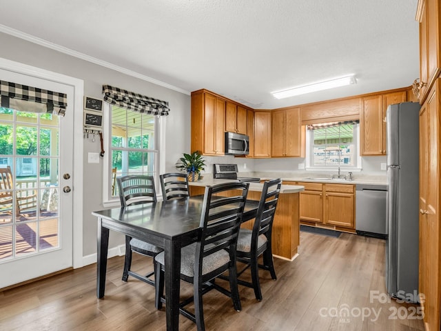 kitchen featuring light countertops, crown molding, stainless steel appliances, a sink, and wood finished floors