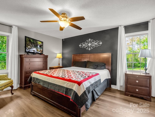 bedroom featuring light wood finished floors, an accent wall, a textured ceiling, and a ceiling fan