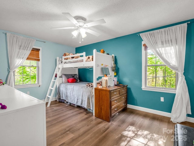 bedroom with a textured ceiling, wood finished floors, baseboards, and multiple windows