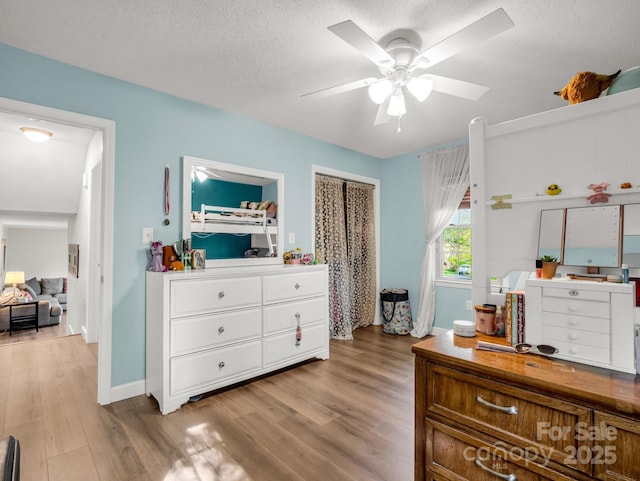 bedroom with a textured ceiling, wood finished floors, baseboards, and a ceiling fan