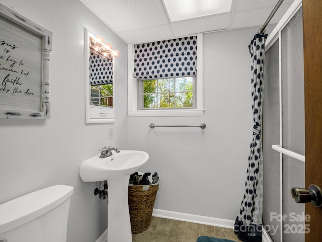 full bath featuring toilet, a drop ceiling, a shower with curtain, and baseboards