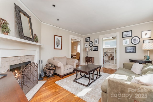living area with wood finished floors, ornamental molding, and a tile fireplace