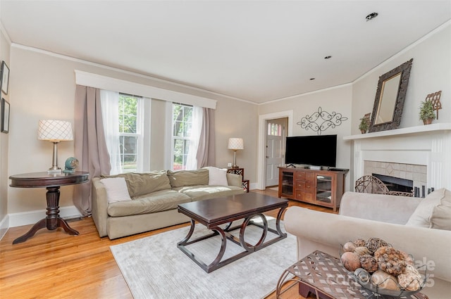 living room featuring wood finished floors, a tiled fireplace, ornamental molding, and baseboards