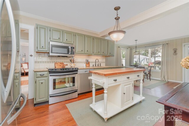 kitchen with crown molding, butcher block counters, light wood-type flooring, appliances with stainless steel finishes, and decorative light fixtures