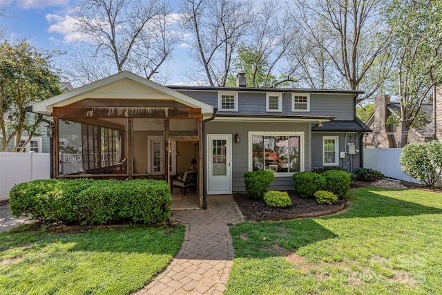 view of front of property featuring a sunroom, a chimney, a front yard, and fence