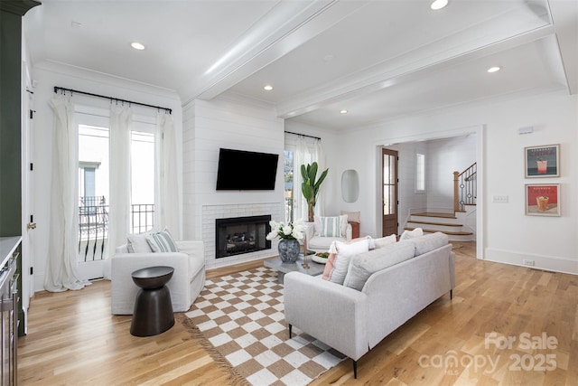 living room featuring a fireplace, stairway, light wood-style flooring, crown molding, and beam ceiling