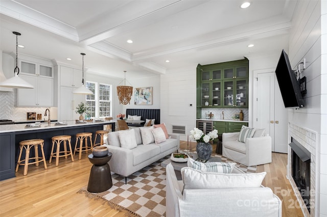living area featuring ornamental molding, beamed ceiling, light wood finished floors, and visible vents
