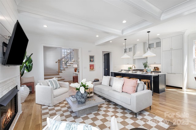 living room featuring a fireplace, stairway, light wood-style flooring, and beamed ceiling