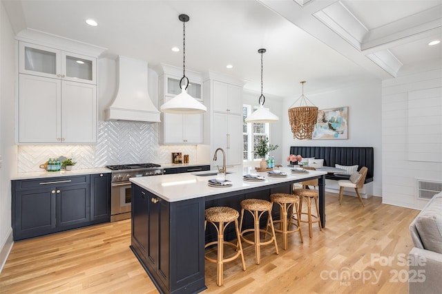 kitchen with custom range hood, high end stainless steel range oven, light wood-style flooring, a kitchen bar, and a sink