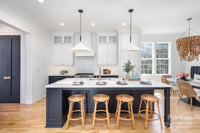 kitchen featuring tasteful backsplash, a sink, light countertops, a kitchen island with sink, and custom range hood
