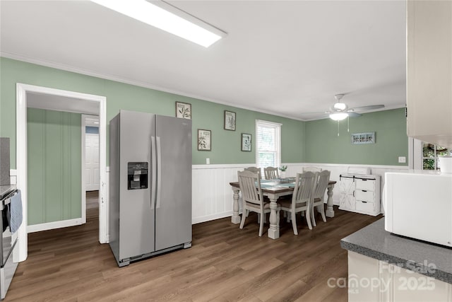 dining space featuring a decorative wall, ornamental molding, a ceiling fan, wainscoting, and wood finished floors