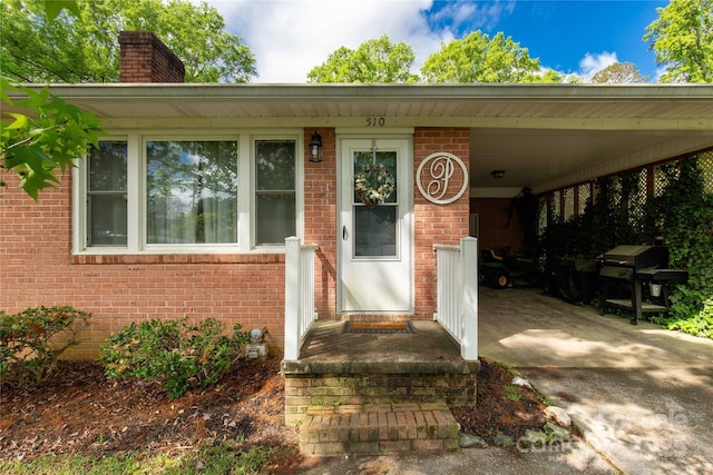 entrance to property featuring brick siding, an attached carport, driveway, and a chimney