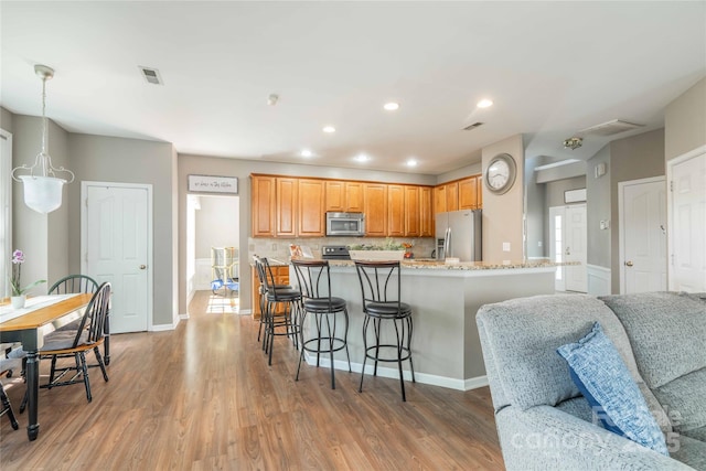 kitchen featuring stainless steel appliances, a breakfast bar, decorative backsplash, and light wood-type flooring