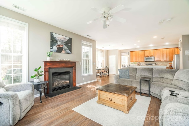 living room with a ceiling fan, visible vents, a fireplace with flush hearth, light wood finished floors, and recessed lighting