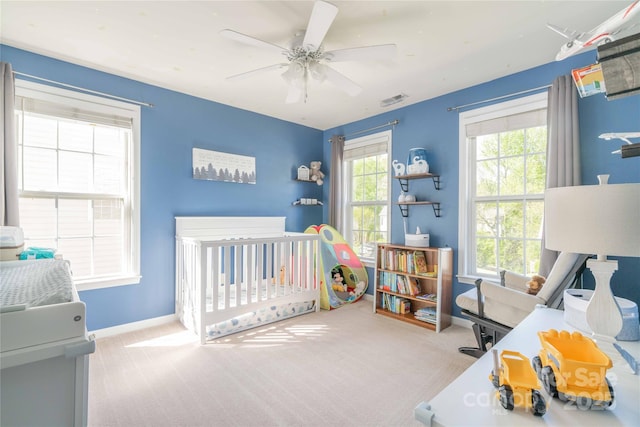 carpeted bedroom with baseboards, visible vents, a crib, and ceiling fan