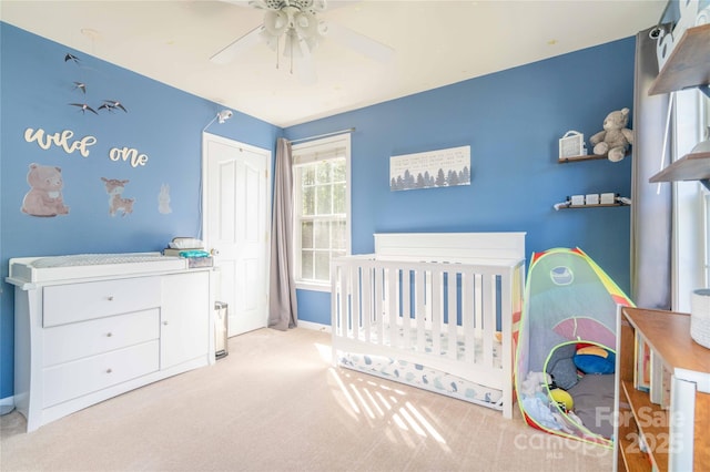 carpeted bedroom featuring a nursery area, baseboards, a ceiling fan, and a closet