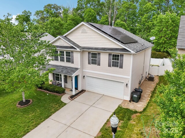 traditional-style house featuring driveway, a front yard, solar panels, a porch, and a garage