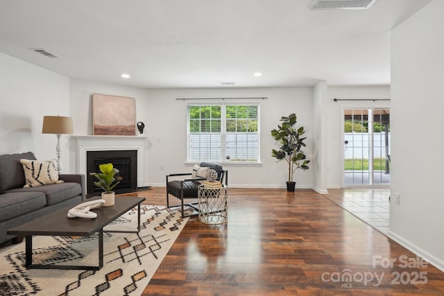 living room featuring recessed lighting, visible vents, a fireplace with flush hearth, and wood finished floors