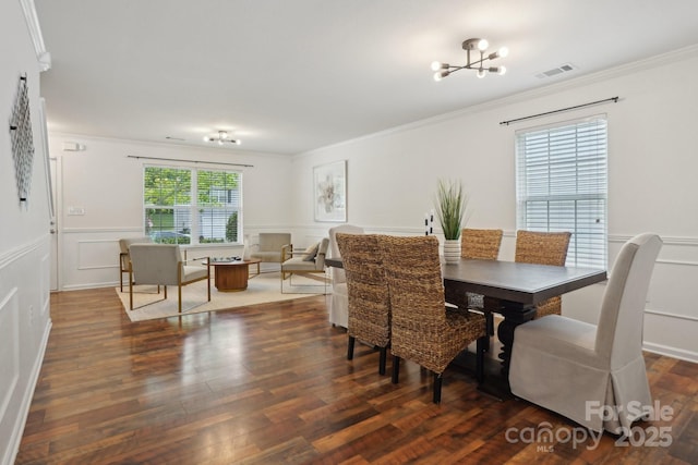 dining area with visible vents, wood finished floors, crown molding, and a decorative wall