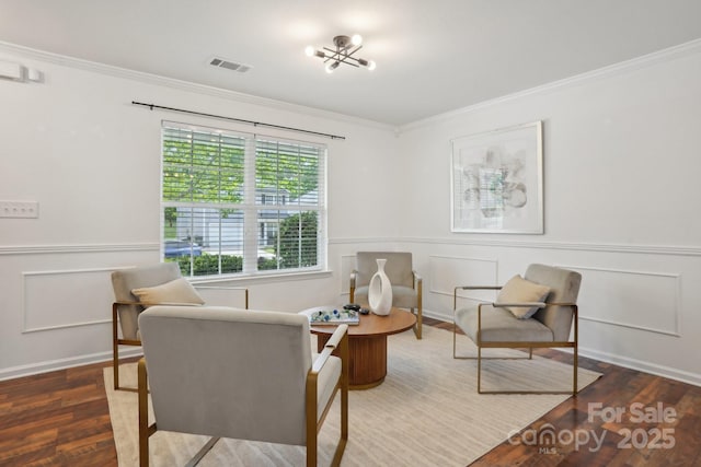 living area with wood finished floors, a decorative wall, ornamental molding, a wainscoted wall, and visible vents