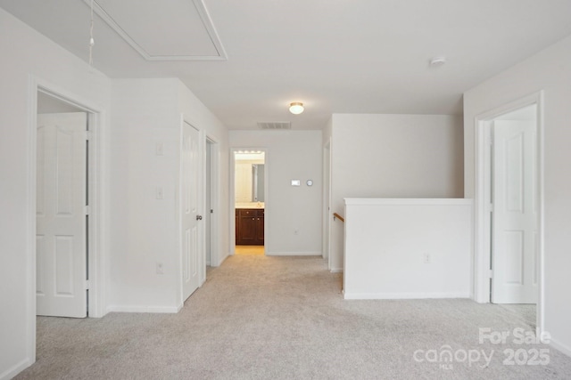 unfurnished room with attic access, visible vents, light colored carpet, and baseboards