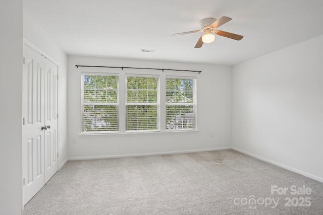 carpeted spare room featuring baseboards, visible vents, and ceiling fan