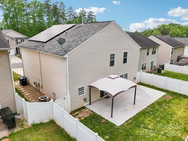 rear view of property with roof mounted solar panels, roof with shingles, a lawn, and a patio