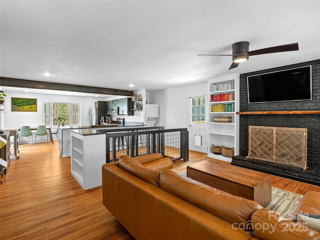 living area with built in features, a brick fireplace, a ceiling fan, light wood-style floors, and a textured ceiling