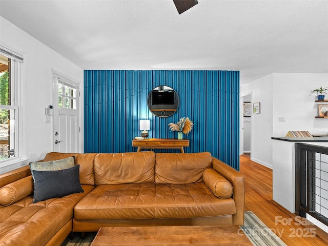 living area with wood finished floors, an accent wall, and baseboards