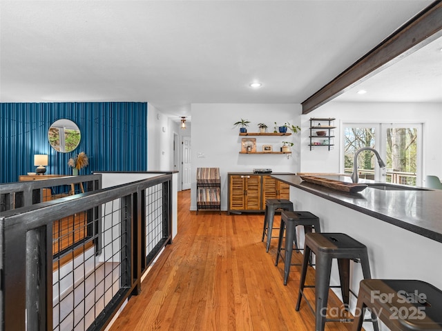 kitchen featuring light wood-type flooring, dark countertops, a kitchen bar, beam ceiling, and a sink