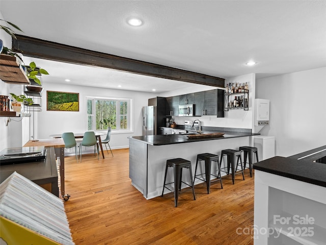 kitchen featuring light wood-style floors, a kitchen bar, a peninsula, dark countertops, and stainless steel appliances