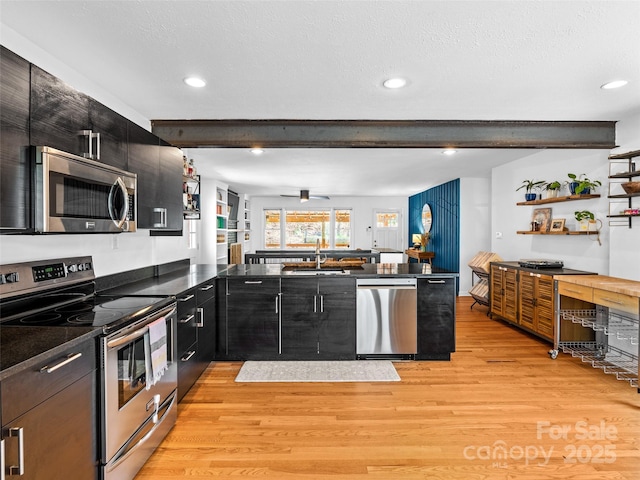 kitchen featuring a sink, appliances with stainless steel finishes, dark cabinets, beam ceiling, and light wood finished floors