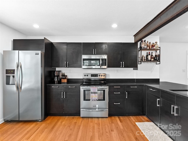 kitchen with dark cabinets, light wood-type flooring, recessed lighting, dark countertops, and stainless steel appliances