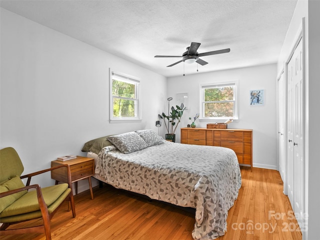 bedroom featuring a closet, baseboards, ceiling fan, light wood-style floors, and a textured ceiling