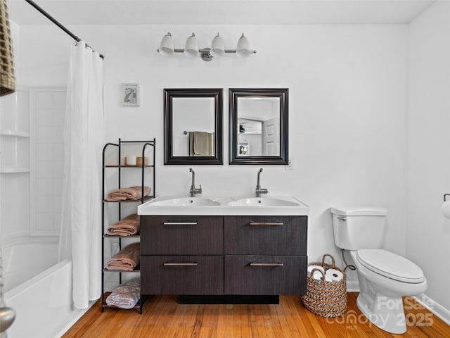 full bathroom with double vanity, toilet, hardwood / wood-style floors, shower / bath combo with shower curtain, and a sink