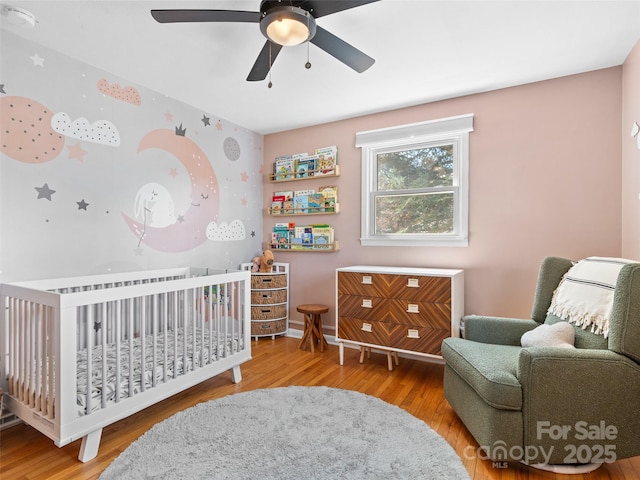 bedroom featuring a nursery area, a ceiling fan, and wood finished floors