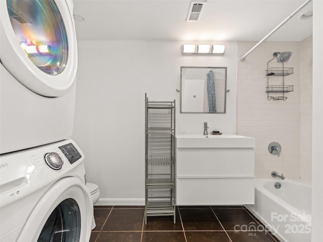 laundry area featuring dark tile patterned floors, stacked washer and dryer, visible vents, laundry area, and a sink