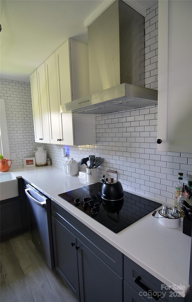 kitchen featuring tasteful backsplash, wall chimney exhaust hood, dishwasher, black electric stovetop, and light wood-style flooring