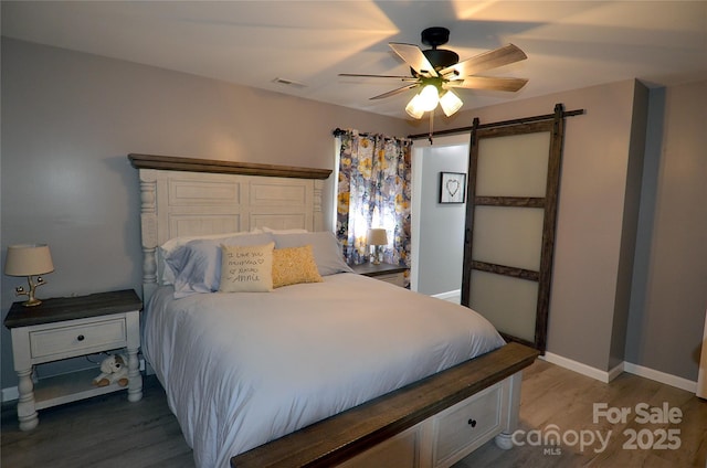 bedroom featuring light wood-type flooring, baseboards, a barn door, visible vents, and ceiling fan