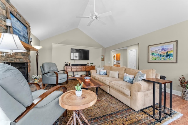 living area featuring lofted ceiling, a stone fireplace, wood finished floors, a ceiling fan, and baseboards