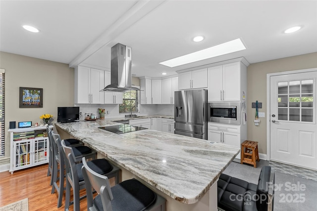 kitchen featuring a skylight, island range hood, a kitchen bar, a peninsula, and appliances with stainless steel finishes